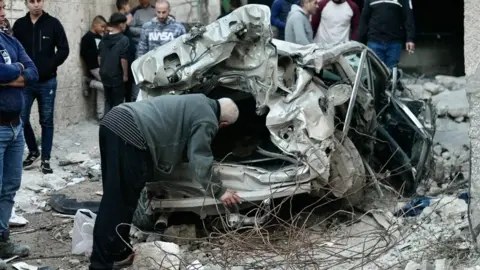 Dave Bull Palestinians inspect a destroyed car in Jenin, in the occupied West Bank, following an Israeli military raid (29 November 2023)