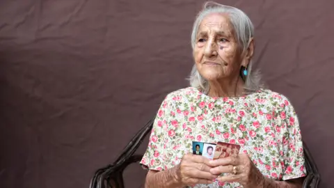 Caritas María Teresa Jimenez holds up photographs of her children