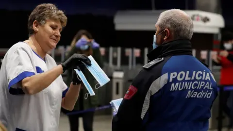 EPA A policeman hands a mask to a commuter at Nuevos Ministerios metro station in Madrid, Spain (13 April 2020)