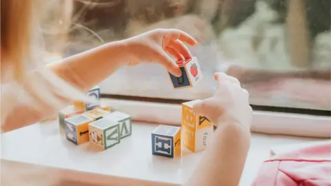 A child plays with small wooden letter blocks on a wood surface