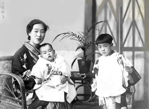 Courtesy of Emiko Okada A woman holds her child, as her other child stands nearby