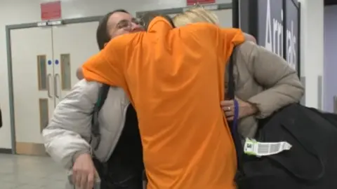 A family hugging after being reunited at Luton Airport