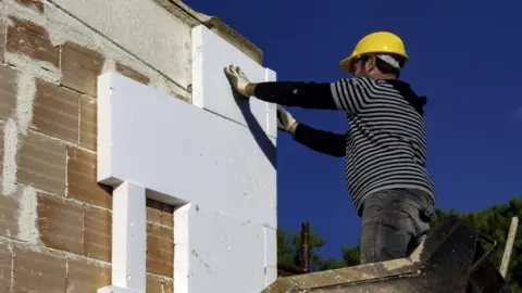 peuceta/Getty Images  A man adding external wall insulation to a house