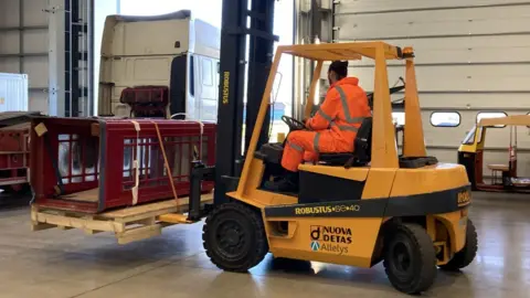 BBC A forklift truck holds up a classic red telephone box.