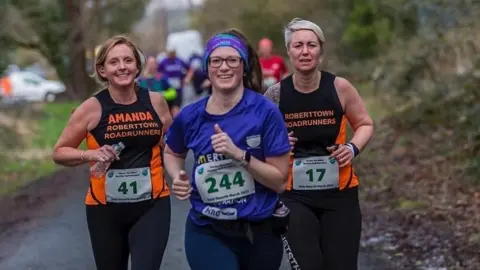 Malcolm John Ruth Coleman in competition kit running on a trail flanked by two other women runners