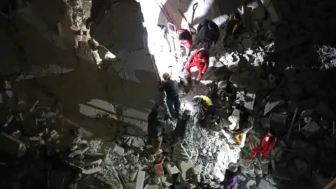 AFP Rescue workers search for survivors in the remains of a block of flats destroyed in a reported air strike in Idlib city (4 February 2018)