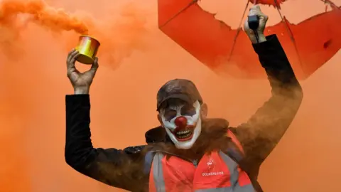 AFP A man wearing a clown mask and waving a smoke bomb takes part in a demonstration to protest against the pension overhauls, in Marseille, southern France, on 5 December, 2019.