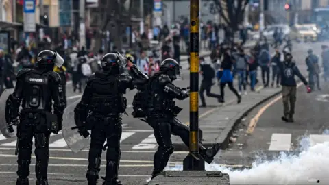 Getty Images A riot policeman kicks a tear gas canister during a protest in Bogota