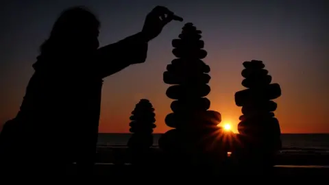 Owen Humphreys/PA Media Woman adds pebble to sculpture as sunrises