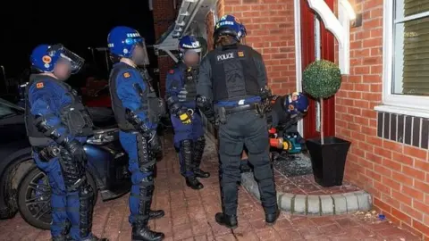 Greater Manchester Police Police officers outside a house trying to get in during a raid