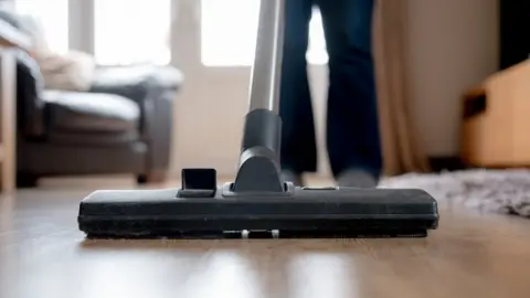 Getty Images Close-up of a vacuum cleaner being used by a blurred figure (legs only visible)