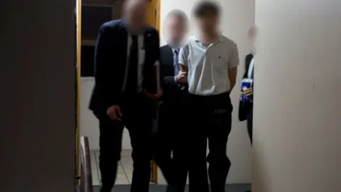 AUSTRALIAN FEDERAL POLICE HANDOUT Man in custody is led down a corridor, but his and officers face is blurred.