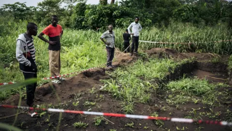 AFP Survivors of an attack in the western village of Bongende, in the Democratic Republic of the Congo, stand on January 27, 2019, next to a mass grave that allegedly contains 100 bodies