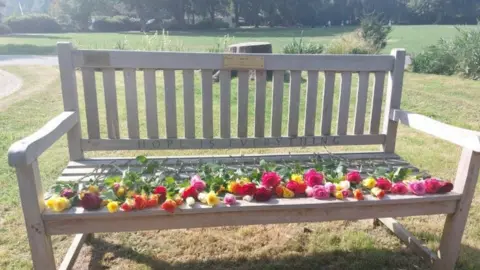 Sammiie White A bench with flowers laid out on it