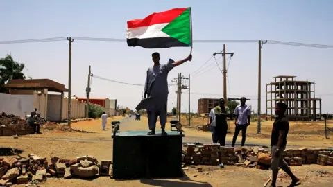 Reuters A Sudanese protester holds a national flag as he stands on a barricade along a street, demanding that the country"s Transitional Military Council hand over power to civilians, in Khartoum, Sudan June 5, 2019.