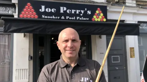 John Devine/BBC Joe Perry stood with a cue outside of his new snooker and pool club