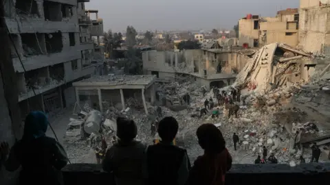 EPA Children look out from their destroyed home as rescue workers search for survivors after air strikes destroyed residential buildings in Hamouria city, in the besieged rebel-held Eastern Ghouta, Syria (9 January 2018)