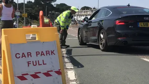 A car park marshal turning a driver away from a full car park