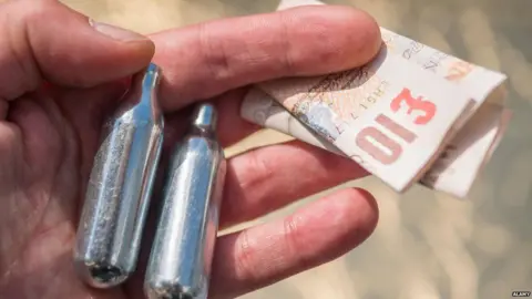 ALAMY Hand holding nitrous oxide canisters and cash