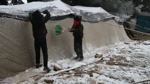 Shafak/CARE Children clear snow off the roof of a tent a camp for displaced people in Aleppo province, Syria