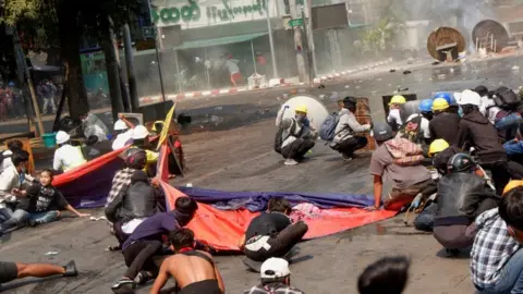 Reuters Protesters crouch after police opened fire to disperse an anti-coup protest in Mandalay, Myanmar