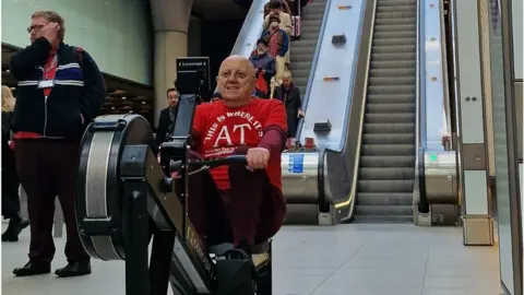 Comic Relief A man uses a rowing machine in a central London underground station