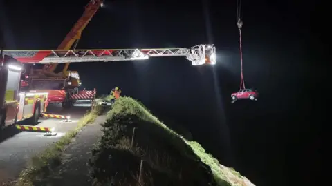 Douglas Coastguard Car hanging from a crane above the cliff edge