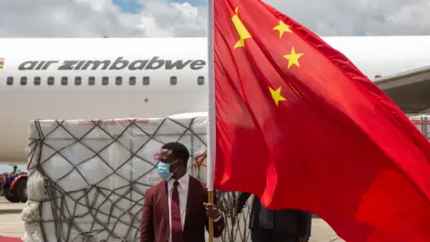 Getty Images A man holds a Chinese flag in front of the shipment of Sinovac and Sinopharm vaccines at Harare International Airport, Zimbabwe - March 2021