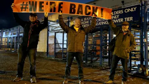 PA Media Luton Town fans pose with a banner prior to the Sky Bet Championship match at Kenilworth Road, Luton