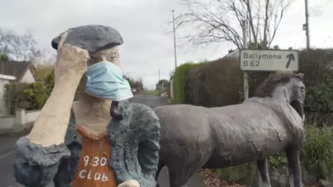 BBC A sculpture of a farmer wearing a surgical mask next to a sculpture of a horse in Cullybackey