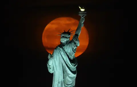 Gary Hershorn / Getty Images The Pink Supermoon rises above the Statue of Liberty in New York City on 27 April 2021