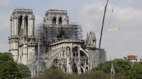 AFP Fire fighters are at work on top of a tower of Notre-Dame Cathedral, as a crane lifts up constreuction material in Paris on April 17, 2019,