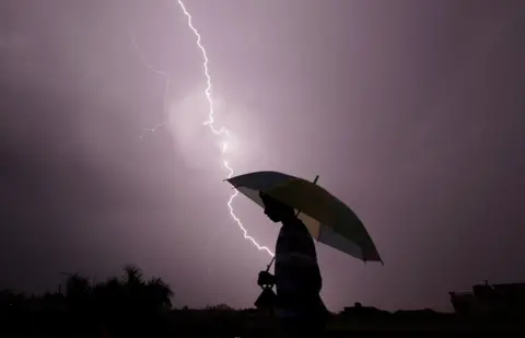 Getty Images A pedestrian walks with an umbrella as lightning strikes during an evening thunderstorm in Jammu on May 14, 2015.