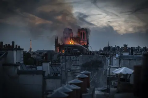 Getty Images Flames and smoke are seen billowing from Notre-Dame's roof