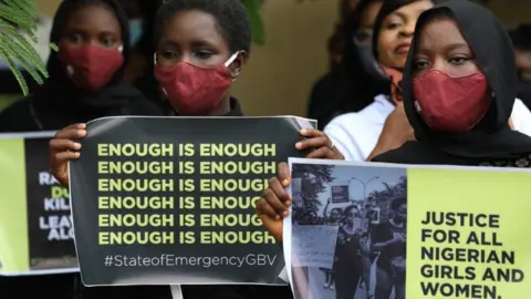 Getty Images Protesters wearing face masks hold banners saying "enough is enough" and "justice in Nigeria for women and girls".