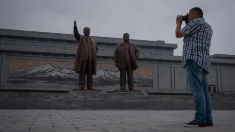 Getty Images A tourist takes a photo of statues of late North Korean leaders Kim Il-Sung (L) and Kim Jong-Il (R), on Mansu hill in Pyongyang on July 23, 2017