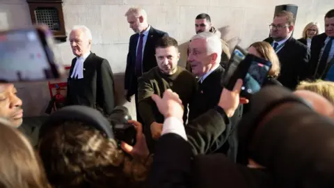 PA Media Ukrainian President Volodymyr Zelensky shakes hands with MPs as he walks with Speaker of the House of Commons, Sir Lindsay Hoyle, and Speaker of the House of Lords, Lord McFall, through the Palace of Westminster.