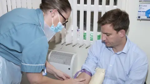 Leicester Biomedical Research Centre Man with short brown hair has his sleeve rolled up whilst a nurse uses a syringe to take a sample