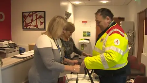 A blood biker hands over a milk delivery