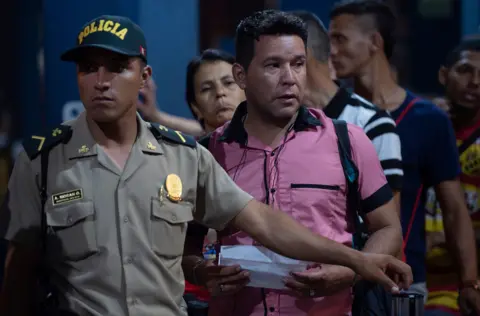 Getty Images A Peruvian policeman assists Venezuelan citizens waiting in line to get a refugee application at a Peruvian border post at the binational border attention centre (CEBAF) in Tumbes on June 14, 2019.