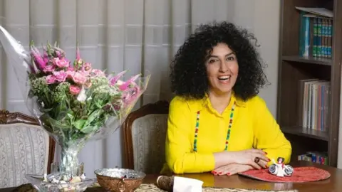 Narges Mohammadi sitting at a desk and wearing a yellow top and colourful necklace