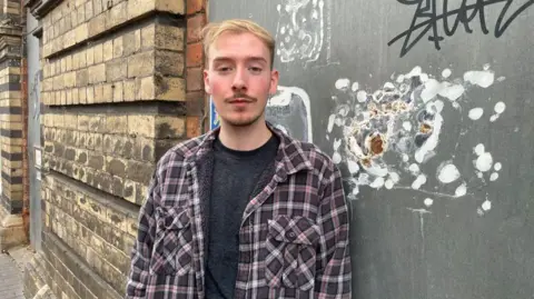 Bridgnorth resident and petitioner Huw Rees looking unhappy in front of the New Market Hall, which has crumbling brickwork and graffiti on a boarded up doorway.
