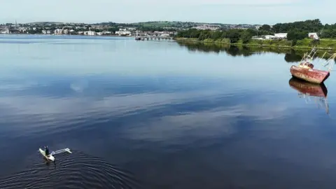 An aerial shot taken over the river foyle showing a ship stuck on a sandbank in the top right and a canoe being paddled up river in the lower left