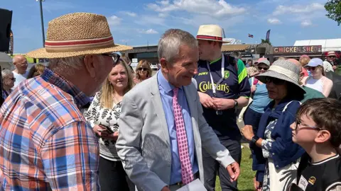 Linsey Smith / BBC Look North presenter Peter Levy surrounded by people at the show. He is wearing a light-coloured suit with pink patterned tie and light blue shirt