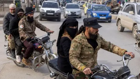 Two groups of people ride along a street on motorbikes in Idlib on 16 December