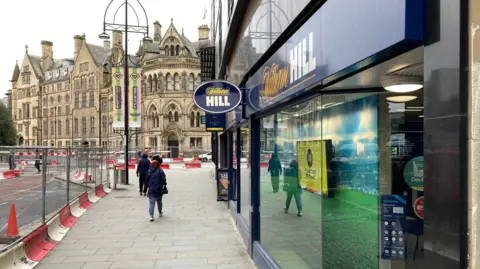 A betting shop in blue livery with the stone Bradford City Hall in the background