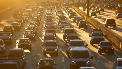 Reuters A freeway crowded with lines of cars, many with headlamps on, all bathed in the orange light of early morning in Los Angeles