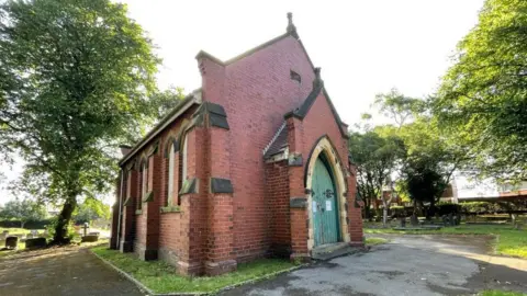 LDRS A small red brick chapel. If has a green arched door at the end and arched windows on the side which are boarded up.