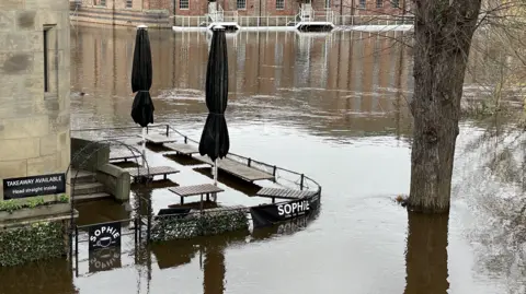 Mark Ansell/BBC An outdoor seating area has been mostly submerged by water, but you can see the tabletops.
