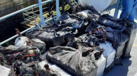 National Crime Agency Blocks of drugs wrapped in black sacking material on board a boat deck